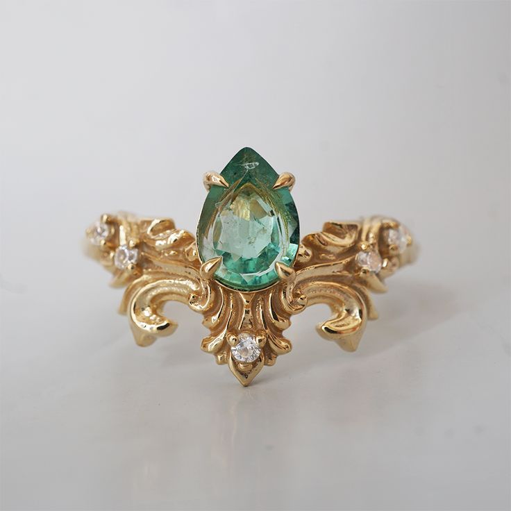 The Achilles Wing Emerald Diamond Ring is a ring that exudes timeless elegance and nature’s grace. At its heart, a pear-shaped, vibrant green emerald shines, symbolizing growth, renewal, and beauty. Surrounding the gemstone is an ornate flourish of gold, meticulously crafted in a floral-inspired design that evokes the grandeur of vintage art and nature's delicate forms. The band designs is inspired by sweeping curves of gilded wings, its design captures a sense of motion and strength, paired wit Elegant Pear-shaped Green Emerald Ring, Elegant Green Pear-shaped Emerald Ring, Elegant Pear-shaped Green Rings, Elegant Green Teardrop Emerald Ring, Teardrop Emerald Green Rings, Teardrop Green Emerald Rings, Green Emerald Teardrop Rings, Green Teardrop Emerald Rings, Teardrop Emerald Ring In Fine Jewelry Style