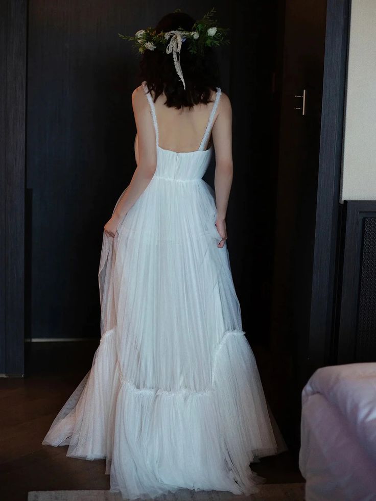 a woman in a white dress is standing near a bed and looking at the door