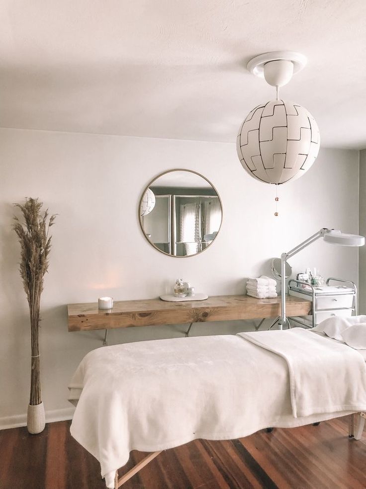 a white bed sitting under a round mirror in a bedroom next to a wooden floor