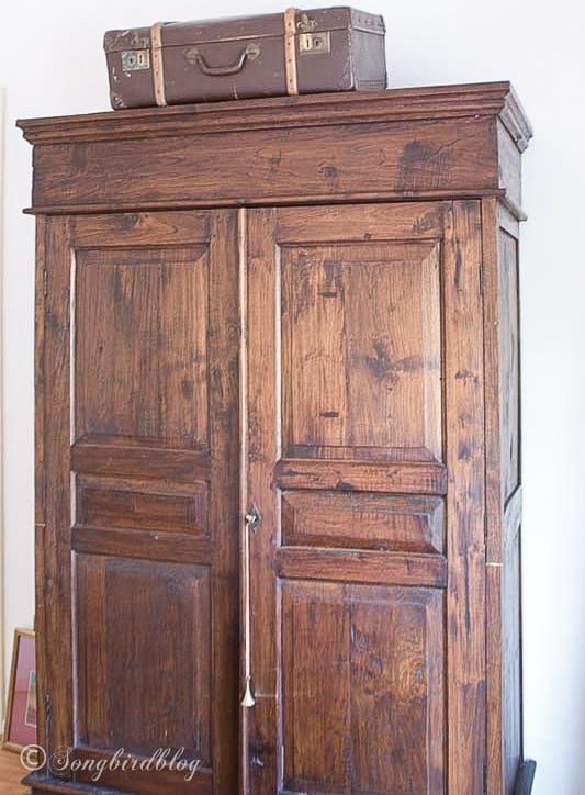 an old wooden armoire with two suitcases on top