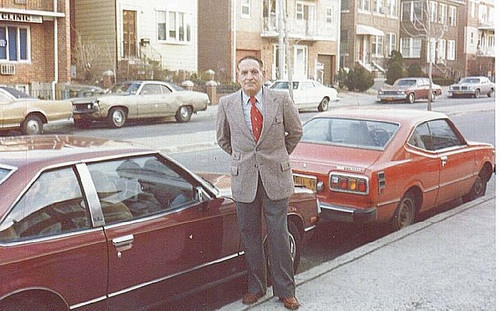 a man in a suit standing next to a red car