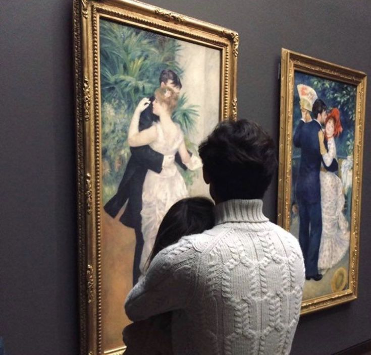 a man and woman looking at paintings on display in an art gallery, with one holding the other's hand