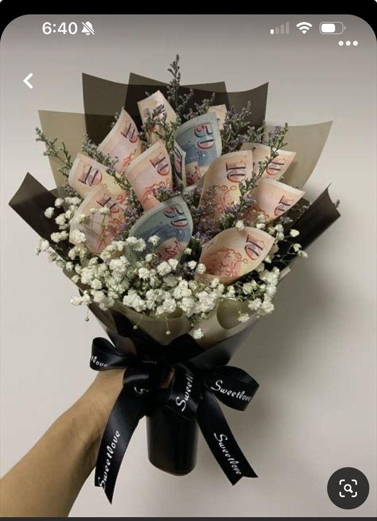 a bouquet of flowers is being held by someone's hand with money notes on it