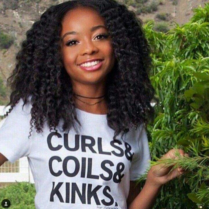 a woman with curly hair wearing a t - shirt that says curls and coils & kinks