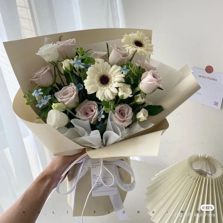 a bouquet of white and pink flowers is being held by a person's hand