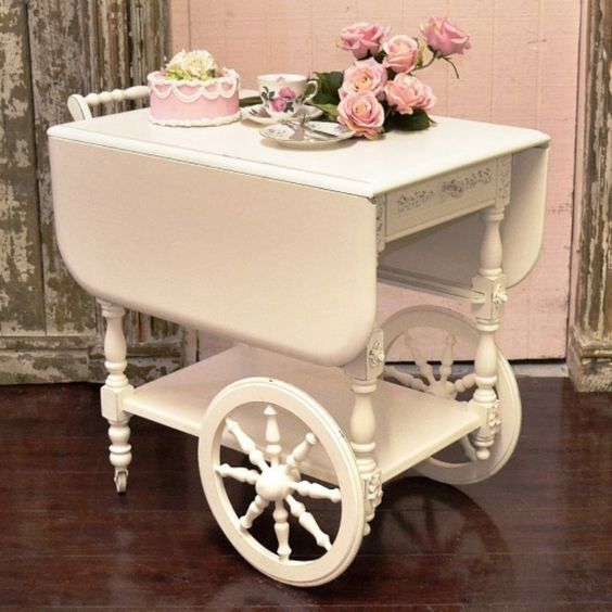 a white cart with pink roses on top and cupcakes in the middle sitting on it