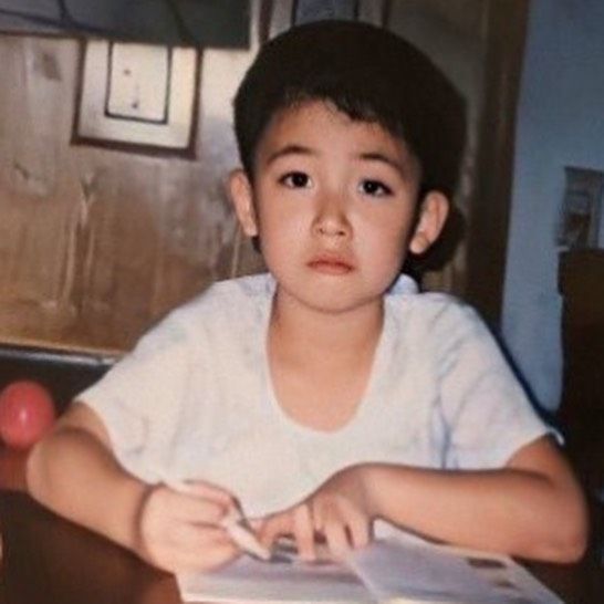 a young boy sitting at a table with papers in front of him and looking off to the side