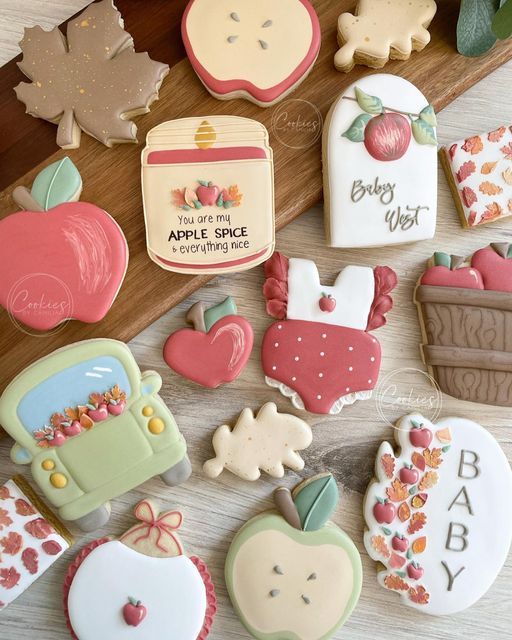 some decorated cookies sitting on top of a wooden table next to leaves and apple slices