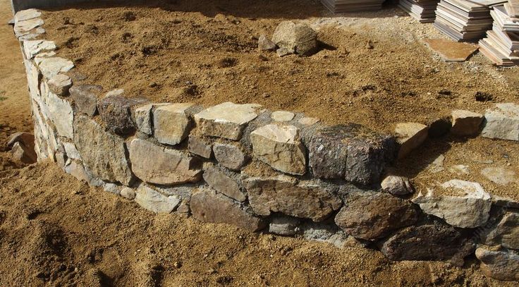 a stone wall in the middle of some dirt and grass next to a building that has been built into it