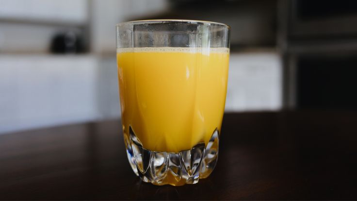 a glass filled with orange juice sitting on top of a wooden table