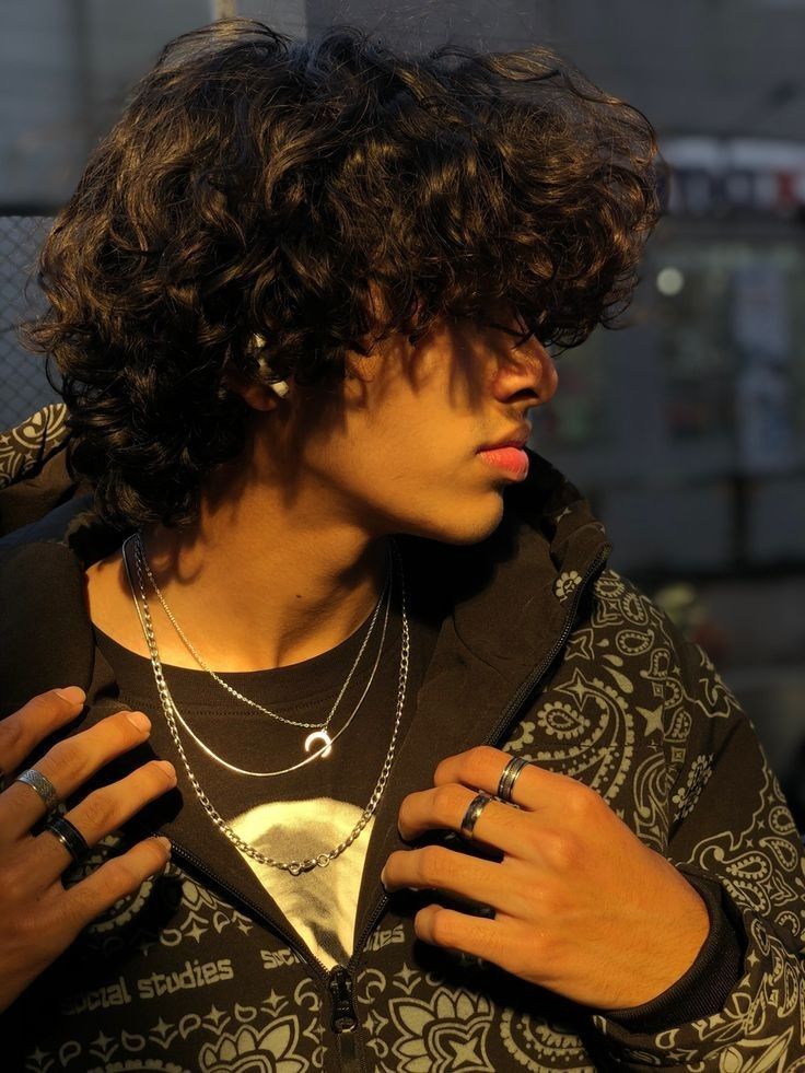 a young man with curly hair and rings on his neck, wearing a black jacket