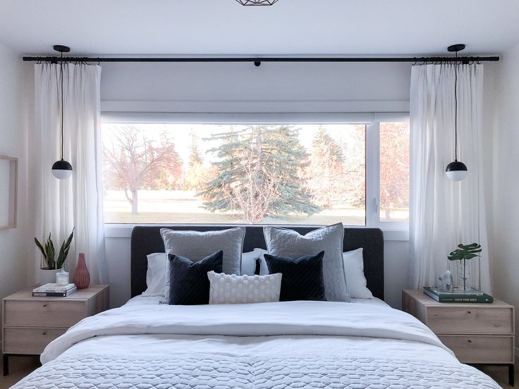 a white bed sitting under a window next to a night stand with two nightstands