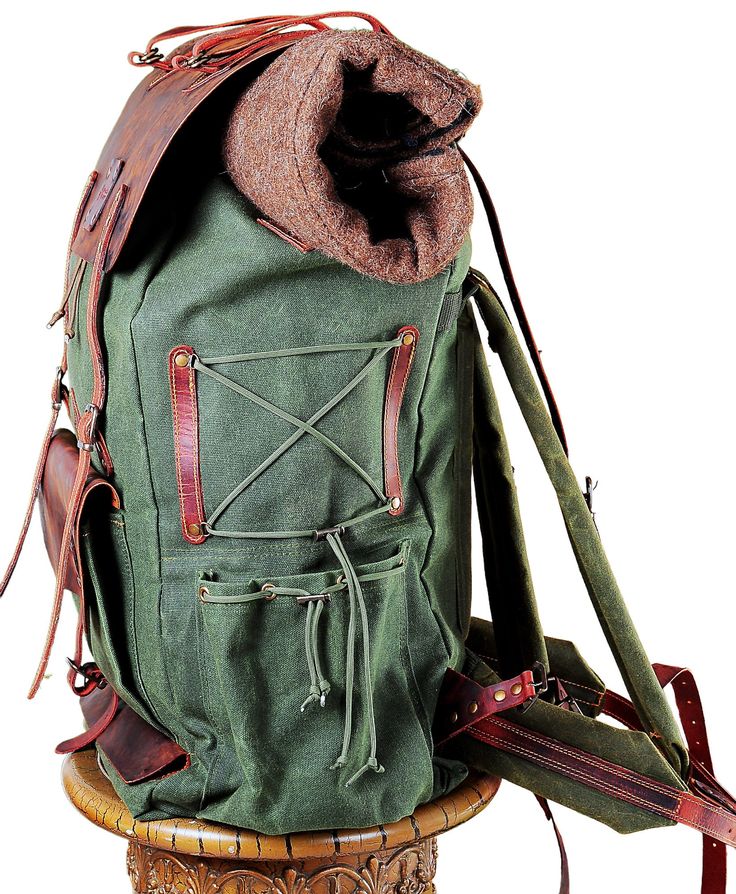 an old green backpack sitting on top of a wooden stool next to a hat bag