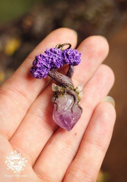 a person holding a tiny purple piece of jewelry in their hand with the flower on it