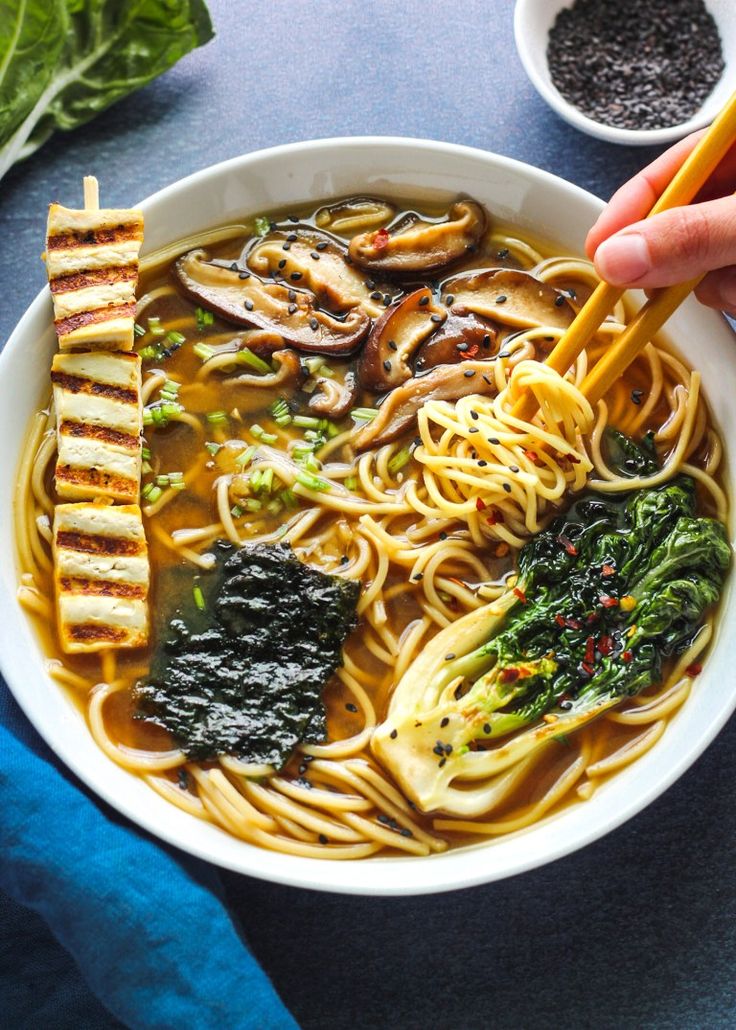 someone holding chopsticks over a bowl of noodles