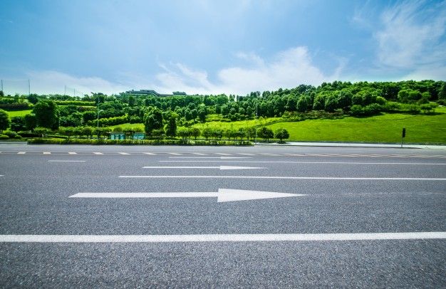 an empty parking lot with two white arrows pointing in opposite directions and trees on the other side