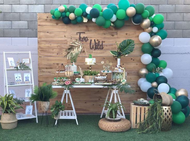 an outdoor party with green and gold balloons, greenery and decorations on the wall