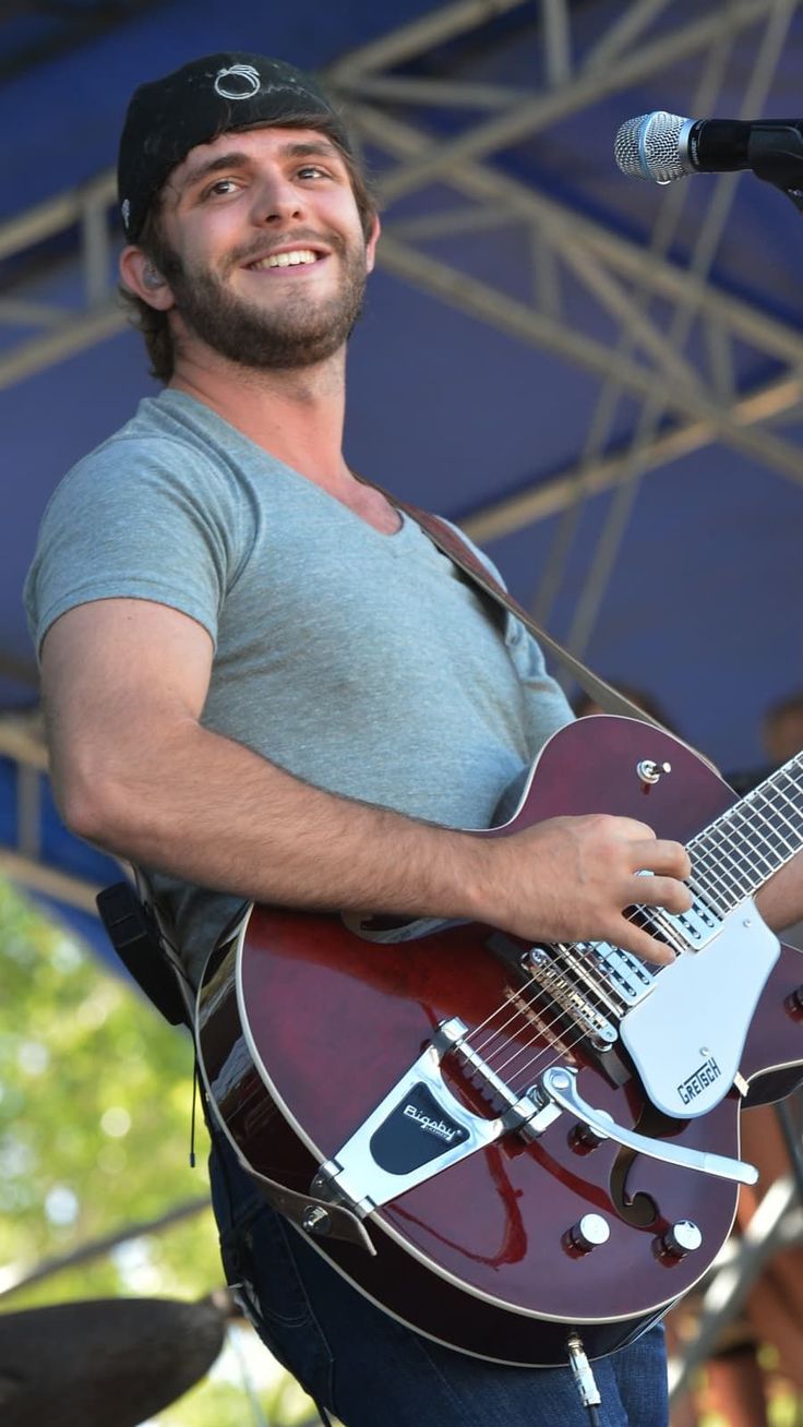 a man holding a guitar and singing into a microphone at an outdoor music festival or concert