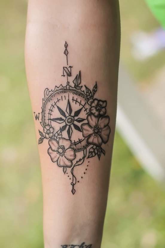 a woman's arm with a tattoo on it that has a compass and flowers