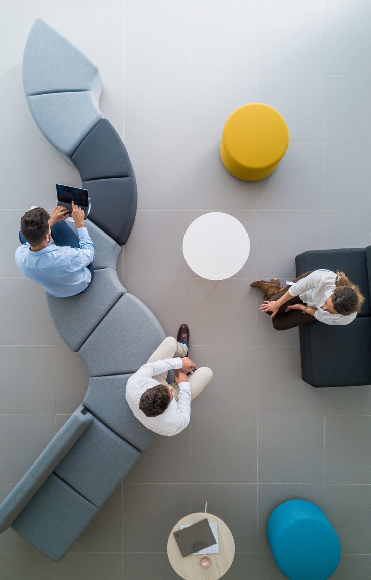 two people sitting on couches in an office with chairs, tables and stools