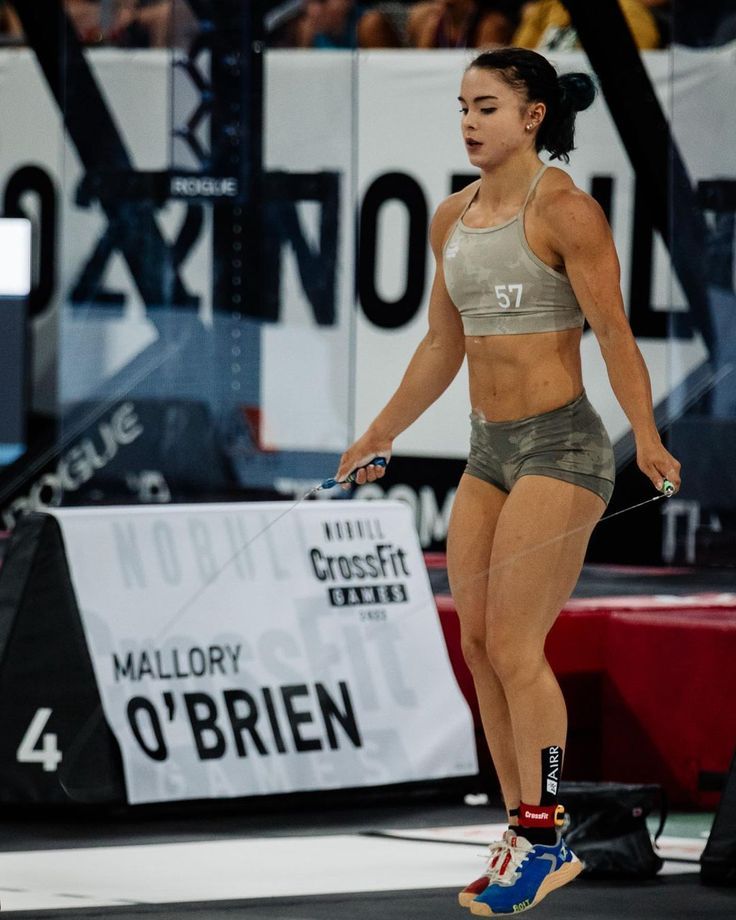 a woman standing on top of a wrestling mat holding a rope in her hand and looking at the ground