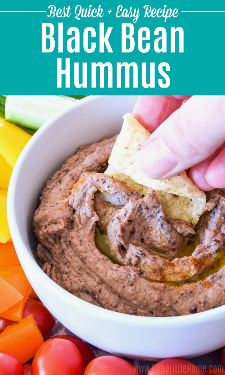 a hand dipping hummus into a white bowl filled with black bean and carrots