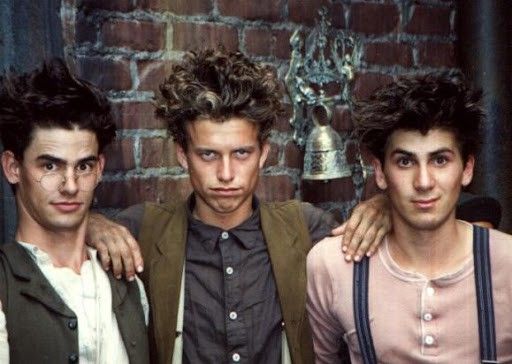 three young men standing next to each other in front of a brick wall and clock