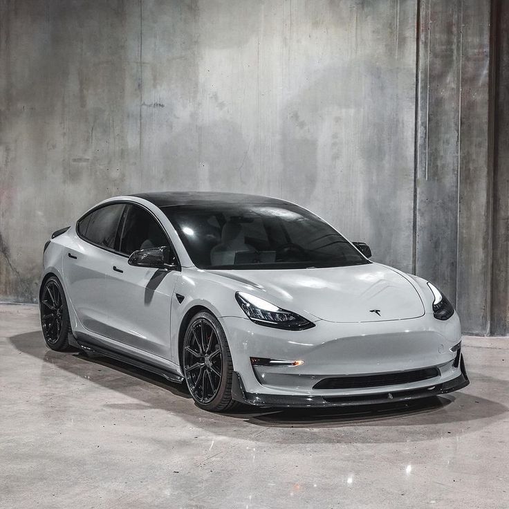 a white tesla model 3 parked in front of a concrete wall with black rims