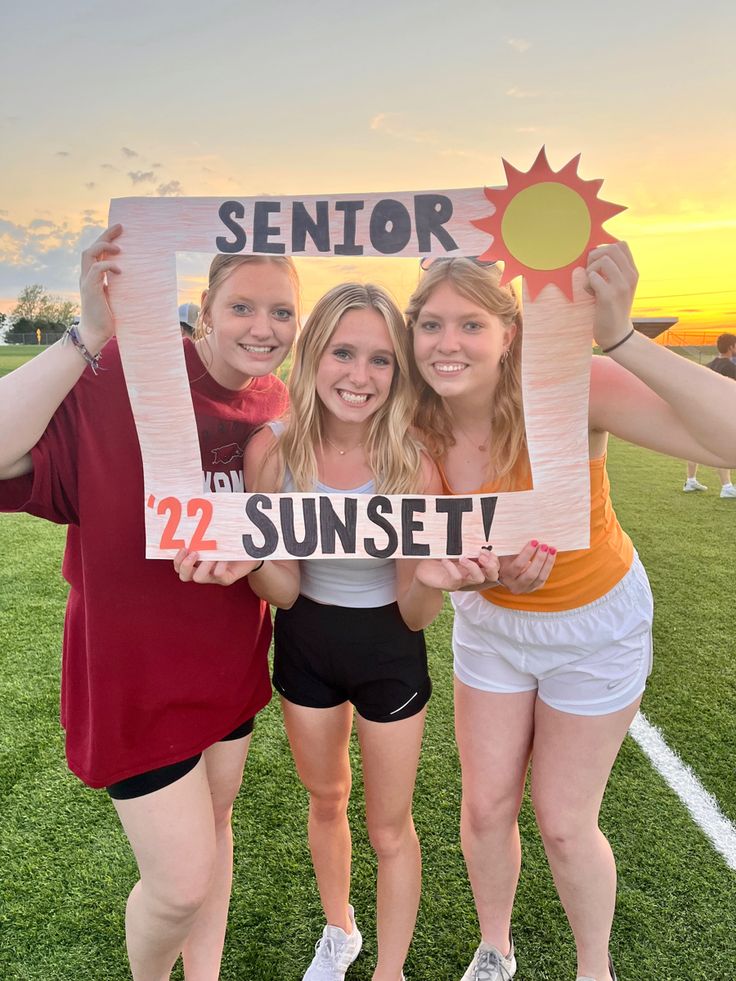 three girls are holding up a sign that says senior 22 sunset on the front and back