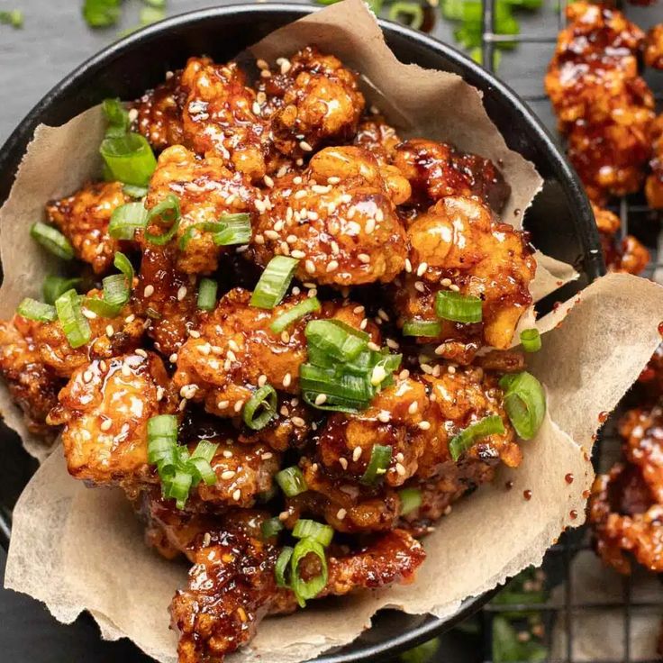 chicken wings with sesame seeds and green onions in a black bowl on top of a table