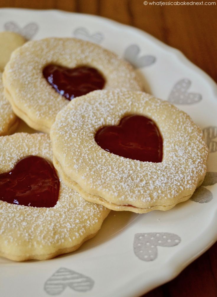 three heart shaped cookies on a plate with powdered sugar and jelly in the middle