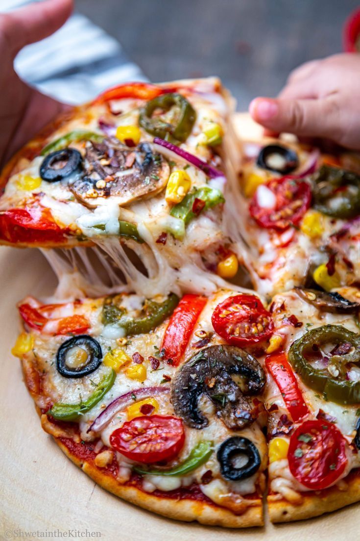 a person is taking a slice of pizza from a wooden platter with several different toppings