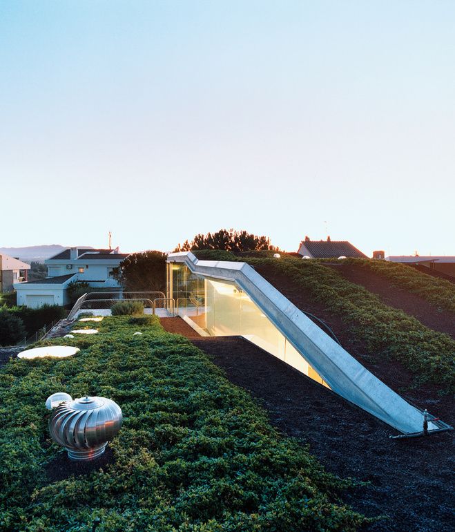 an unusual house that is on top of a hill with grass growing all around it