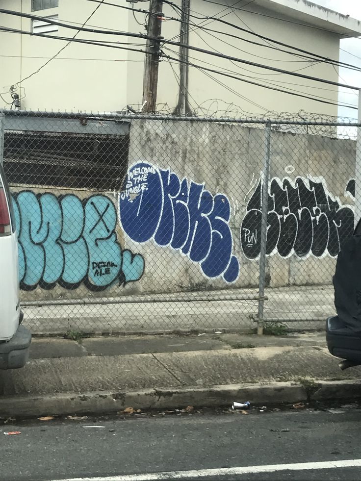 a man sitting on the curb next to a fence with graffitti on it