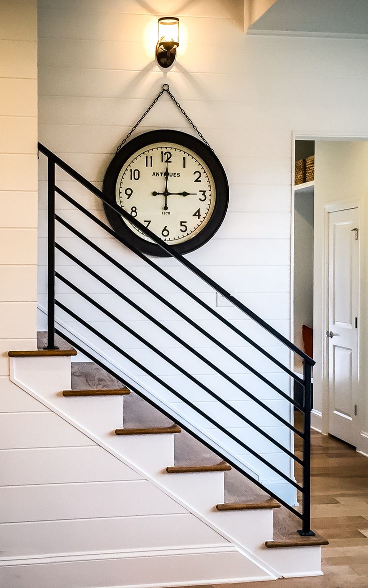 a clock hanging on the wall next to a stair case with railings and handrail