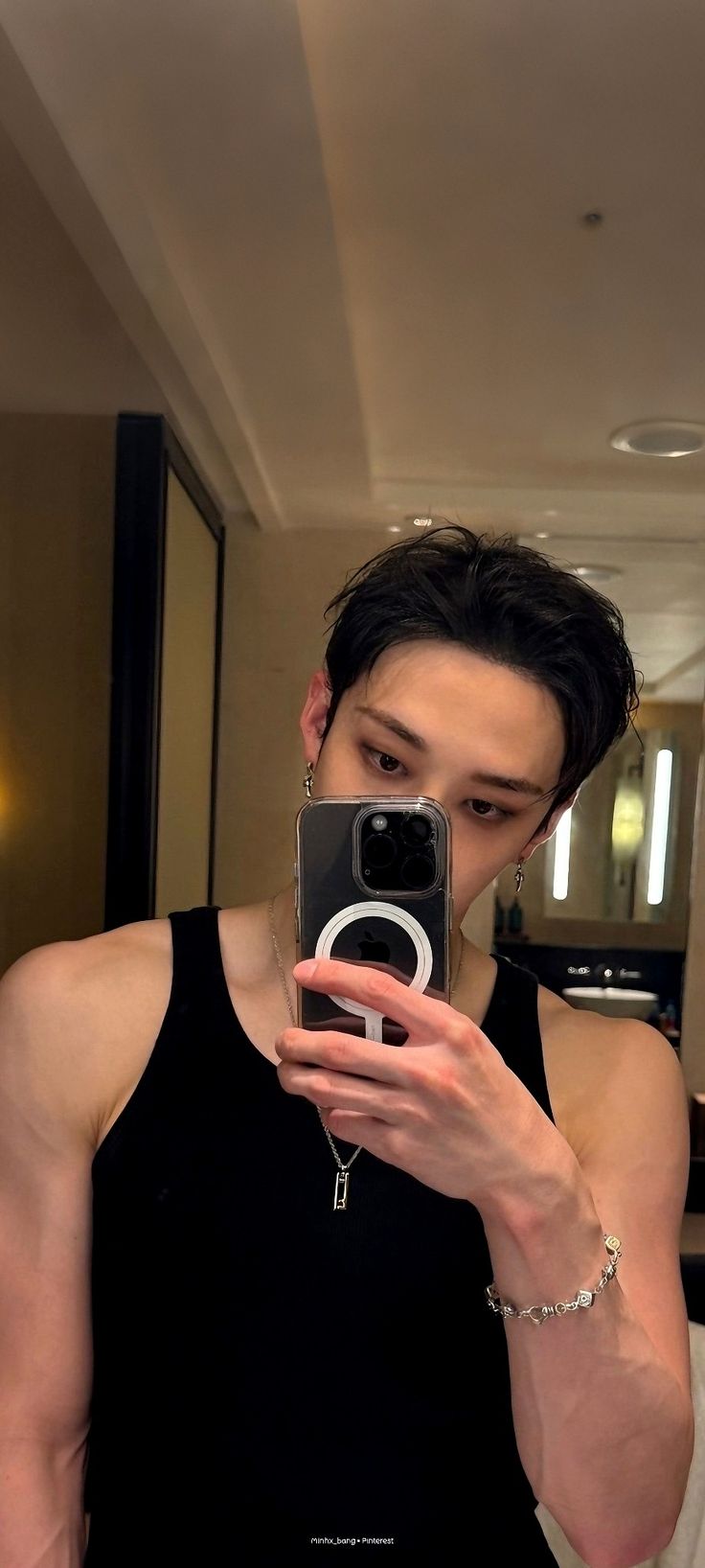 a young man taking a selfie with his cell phone in the bathroom while wearing a black tank top