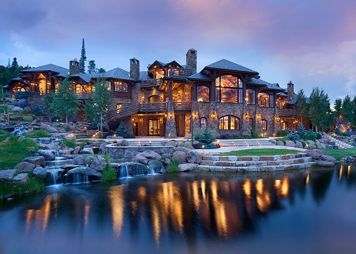 a large stone house sitting on top of a lush green hillside next to a lake