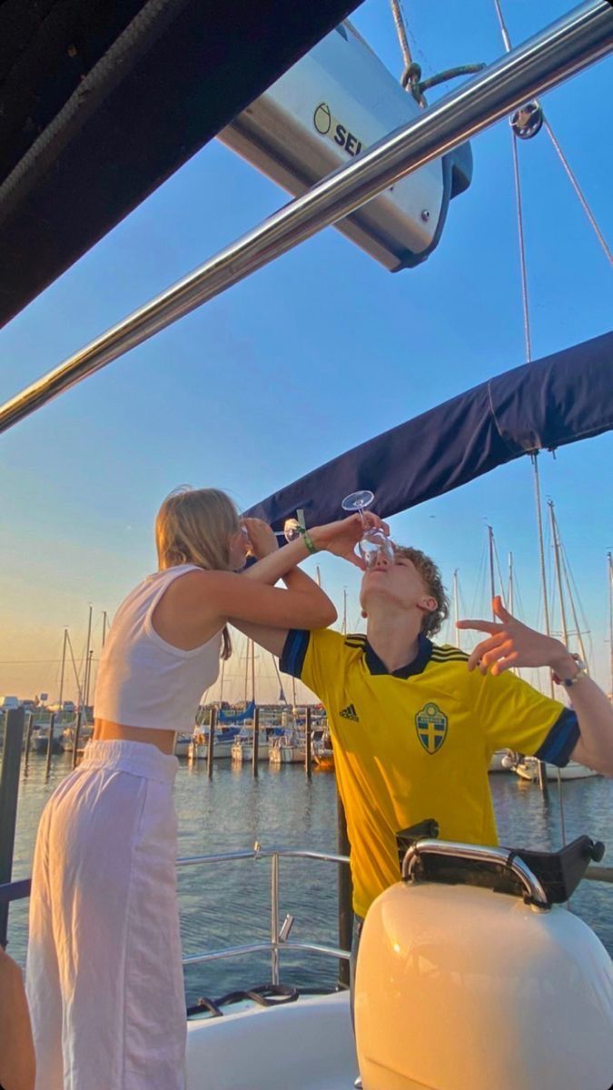 two people standing on the deck of a boat drinking from wine glasses while another person holds his hand up