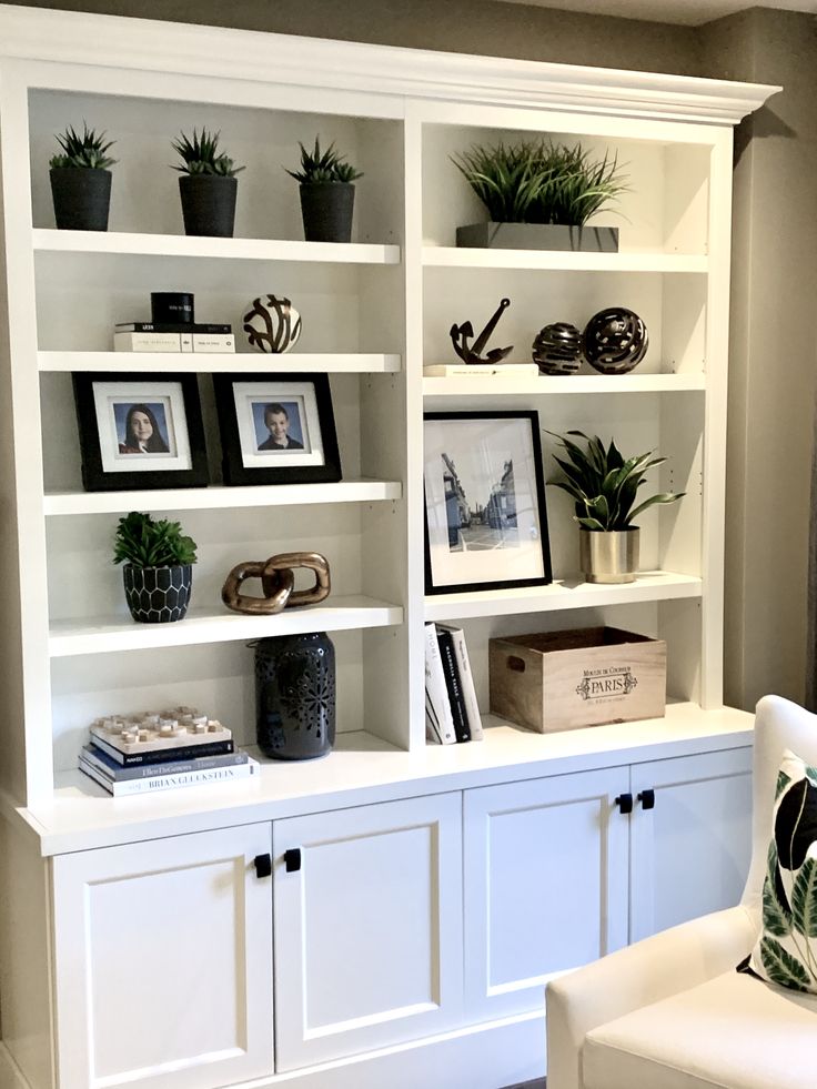 a white bookcase with plants and pictures on it