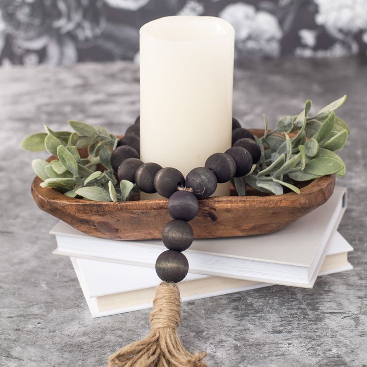 a white candle sitting on top of a wooden bowl filled with black beads and greenery