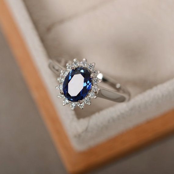 a ring with a blue stone surrounded by white diamonds in a wooden box on the floor