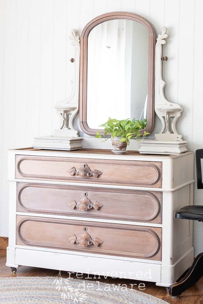 a white dresser with a mirror on top of it and a plant in the corner