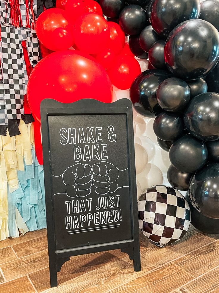 a chalkboard sign sitting on top of a wooden floor next to balloons and streamers