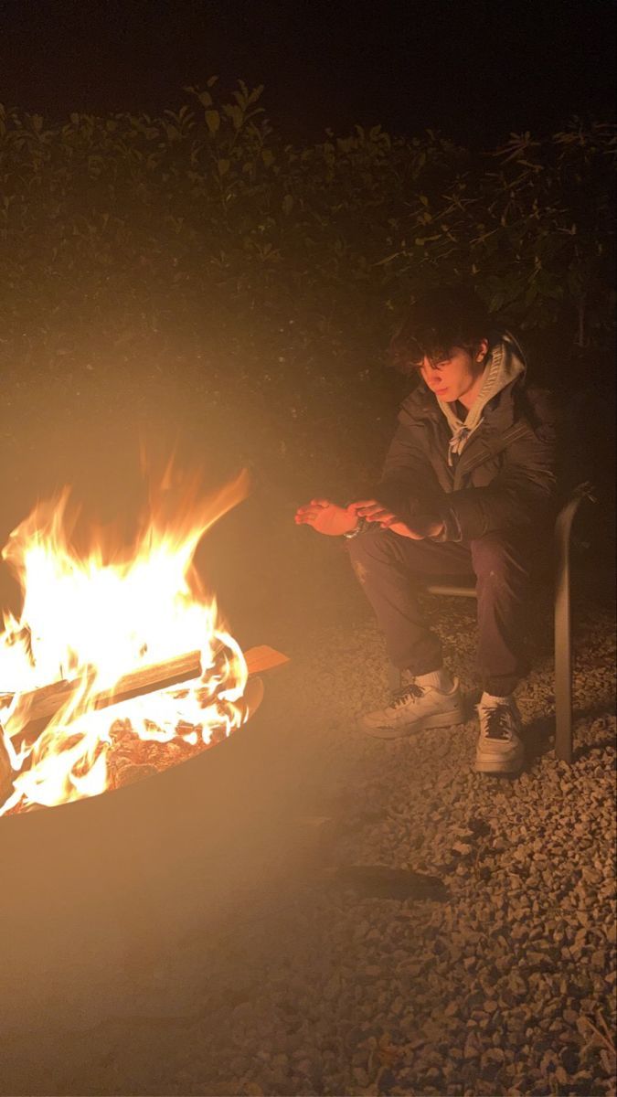 a man sitting in front of a fire with his hand on the ground next to it