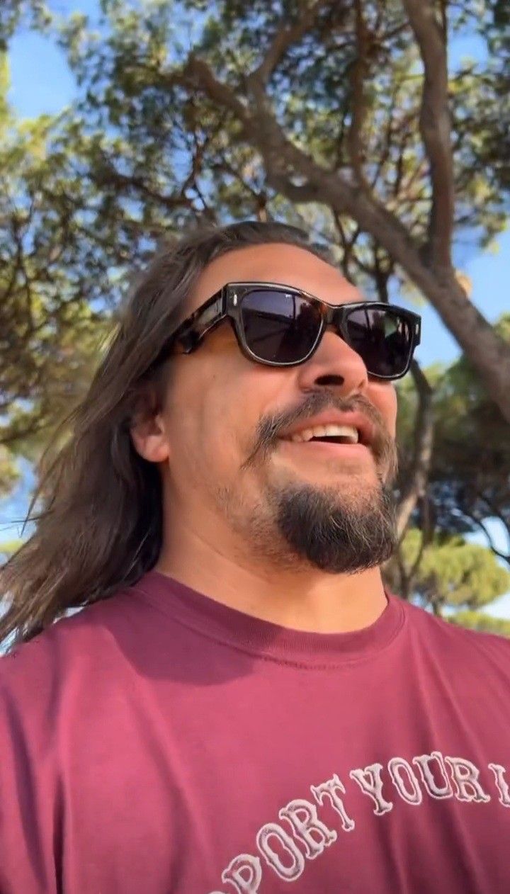 a man with long hair and sunglasses looking up at the sky in front of trees