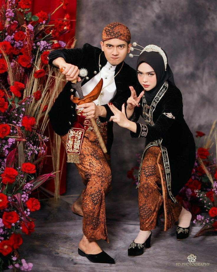 two people dressed in costume posing for a photo with red flowers and roses behind them