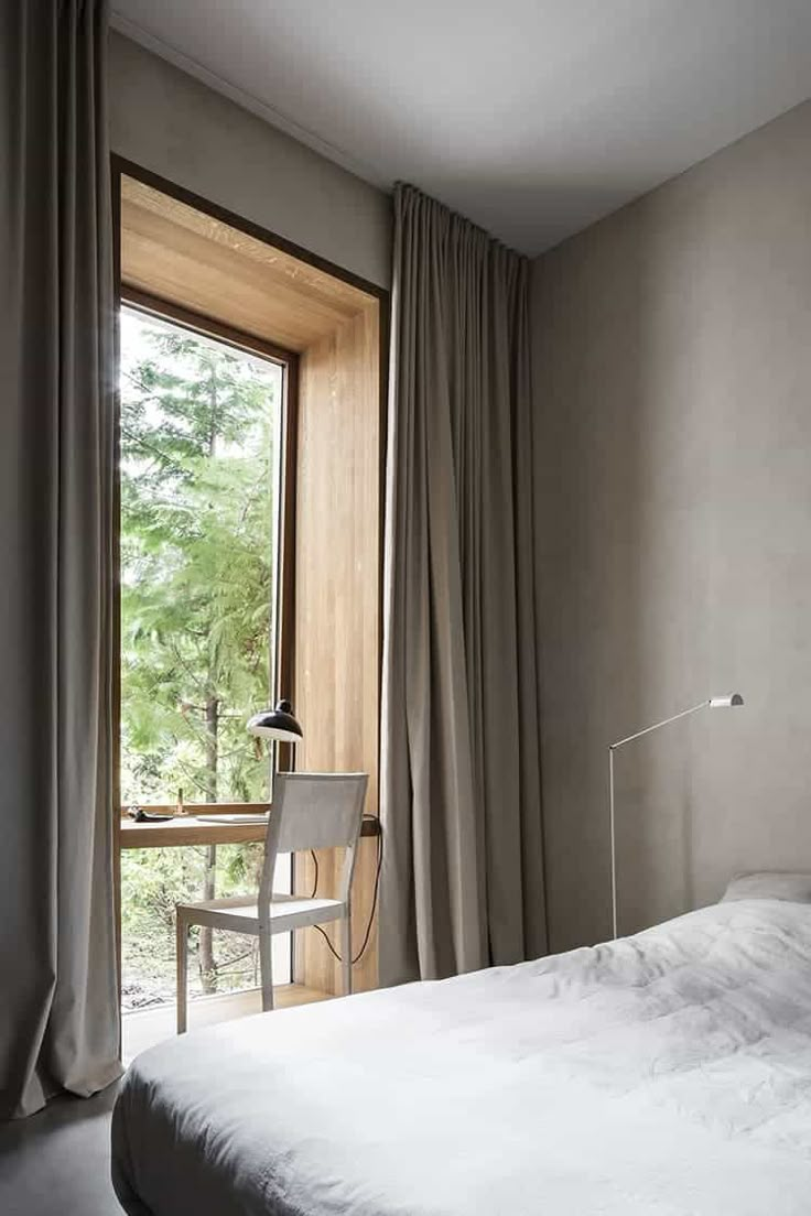 a bed sitting next to a window in a room with curtains on the windowsill