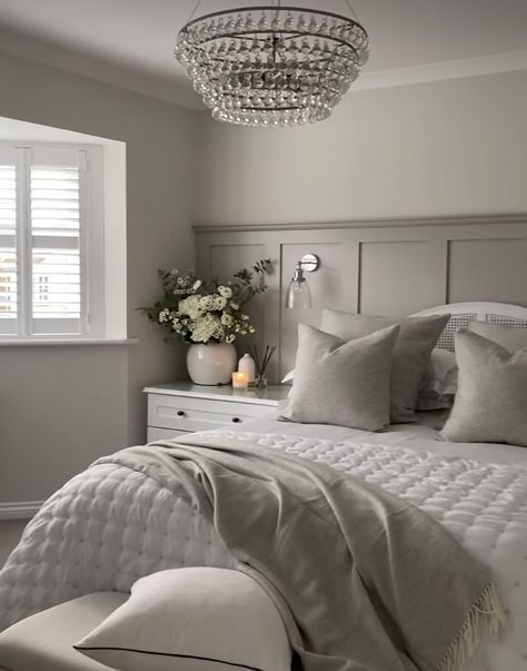 a white bed sitting under a chandelier in a bedroom next to a window