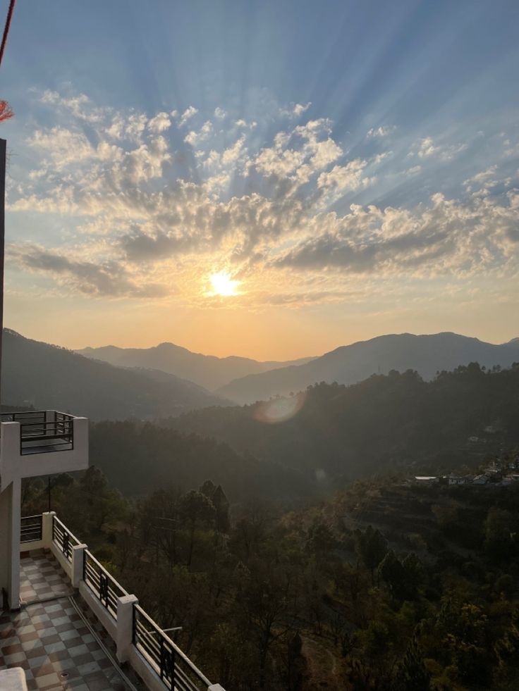 the sun is setting over some mountains and hills in the distance, with a balcony on one side