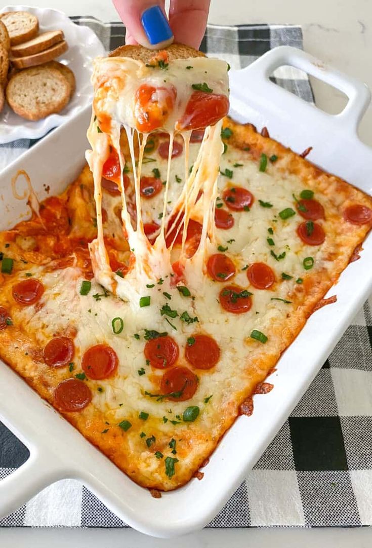 a slice of pepperoni pizza being lifted from a casserole dish with crackers on the side